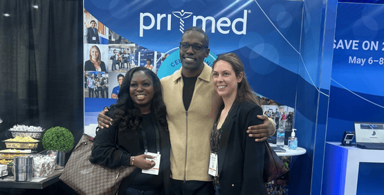Dr. Sutton greeting two attendees at the Pri-Med booth and posing for a picture.