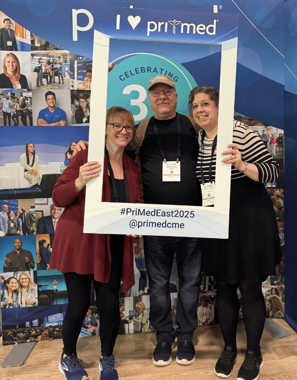Three attendees posing with a photo frame that says "I [heart] Pri-Med"